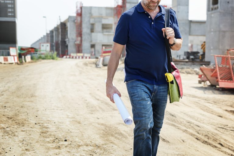 Inżynier z planami na placu budowy – firma budująca drogi nadzoruje przebieg inwestycji