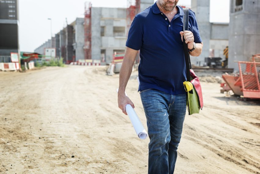 Inżynier z planami na placu budowy – firma budująca drogi nadzoruje przebieg inwestycji