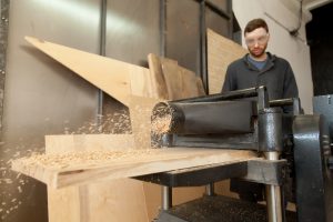 Producent łóżek drewnianych wykonujący obróbkę desek w profesjonalnym warsztacie stolarskim